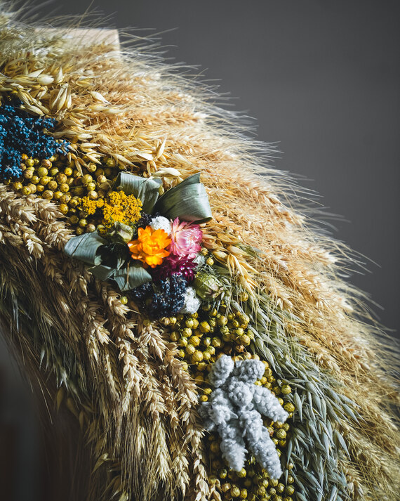 Detail eines Erntekranz aus Getreide und bunten Trockenblumen